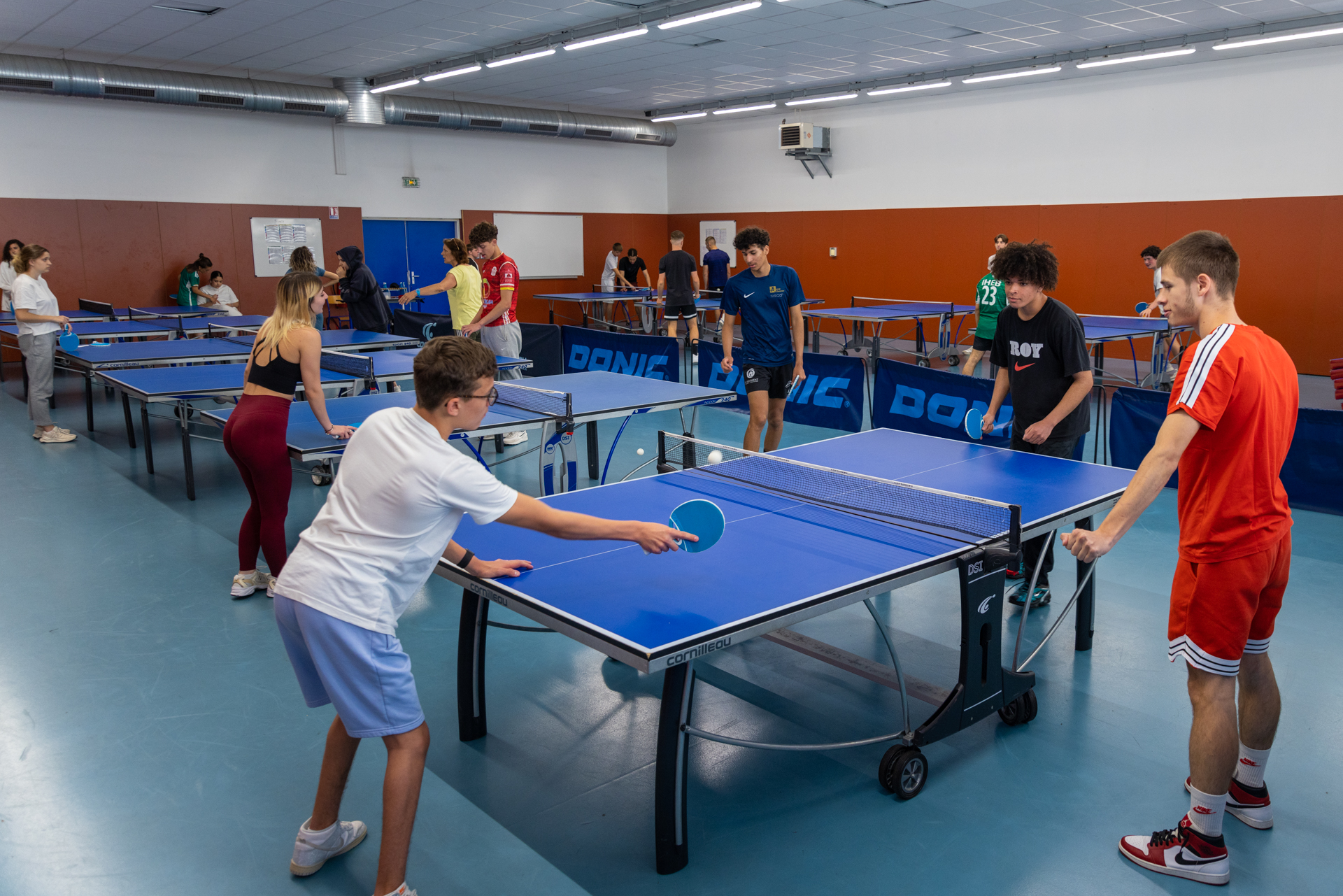 Des élèves et étudiants pratiquent le tennis de table dans la salle sportive du lycée